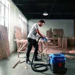 Aspirateur industriel Bosch GAS 12-25 PL Bleu/Noir 200 kPa 1250W, en action: opérateur coupe du bois en atelier relié à