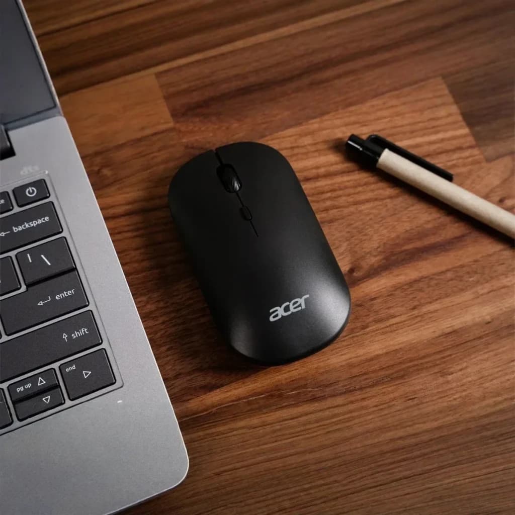 Souris Acer AMR130 Noir Sans Fil Dual Mode, vue dessus: sur bureau en bois à côté d'un laptop et d'un stylo