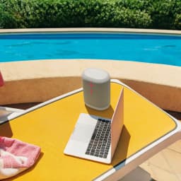 Enceinte portable Ultimate Ears Epicboom IP67 17h Bluetooth Blanc, en utilisation: sur table jaune près d'un laptop au bord