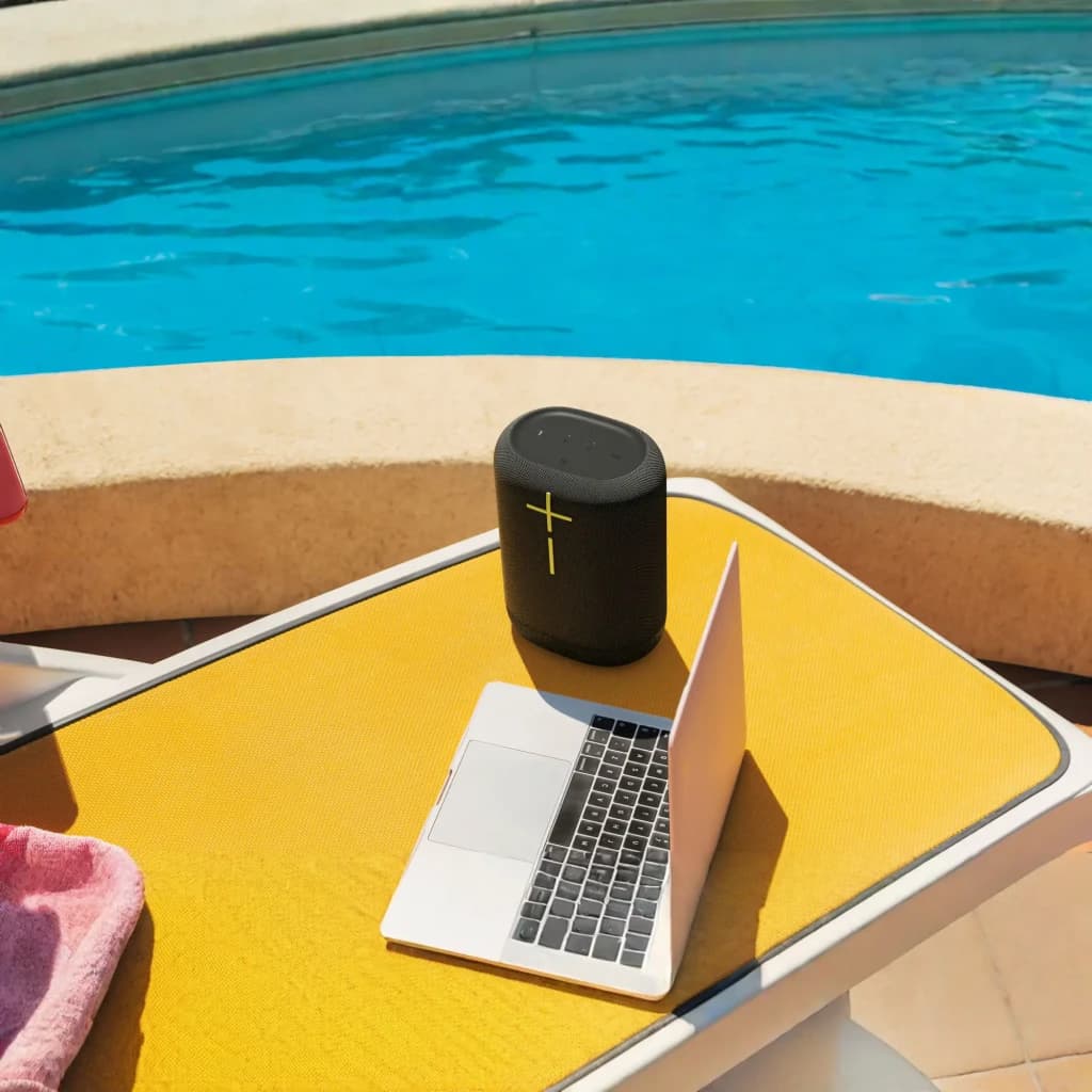 Altavoz portátil Ultimate Ears Epicboom IP67 17h Bluetooth Negro, en uso: sobre mesa junto a piscina con portátil, botones