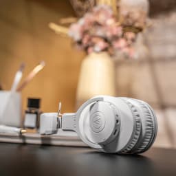 Casque Audio-Technica ATH-M20xBT Supra-auriculaire Bluetooth 5.0 60h Blanc, en situation: replié sur bureau avec vase doré