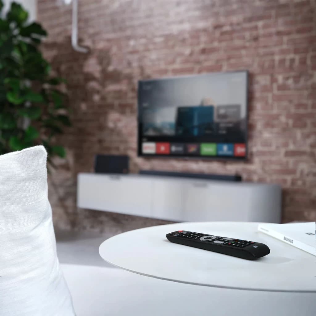Mando Universal One for All Evolve 2 URC7125 IR Inalámbrico, en uso: mando negro sobre mesa blanca con TV encendida al fondo