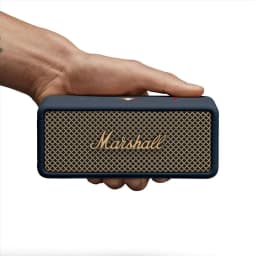 Coluna portátil Marshall Emberton III IP67 32h Bluetooth 5.3 Azul Meia-Noite, em uso: mão a segurá-la, grelha dourada