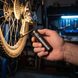 Linterna LED Flextail Zero 1200 Negra Recargable USB-C IP67, en uso: mano sujetándola en taller de bicicletas, logo