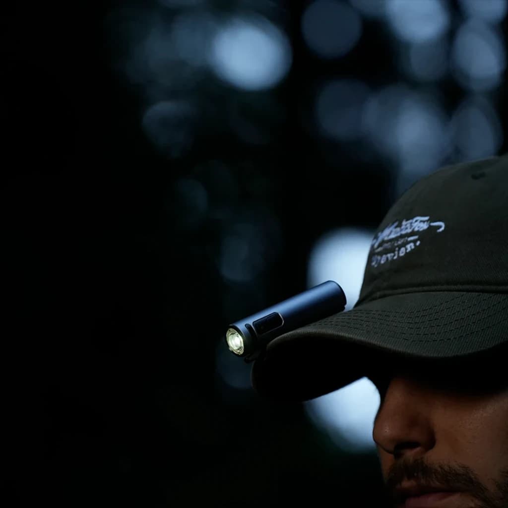 Linterna LED Flextail Zero 1200 Negra Recargable USB-C IP67, en uso: sujeta con clip en visera de gorra, encendida