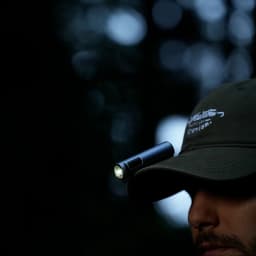 Linterna LED Flextail Zero 1200 Negra Recargable USB-C IP67, en uso: sujeta con clip en visera de gorra, encendida