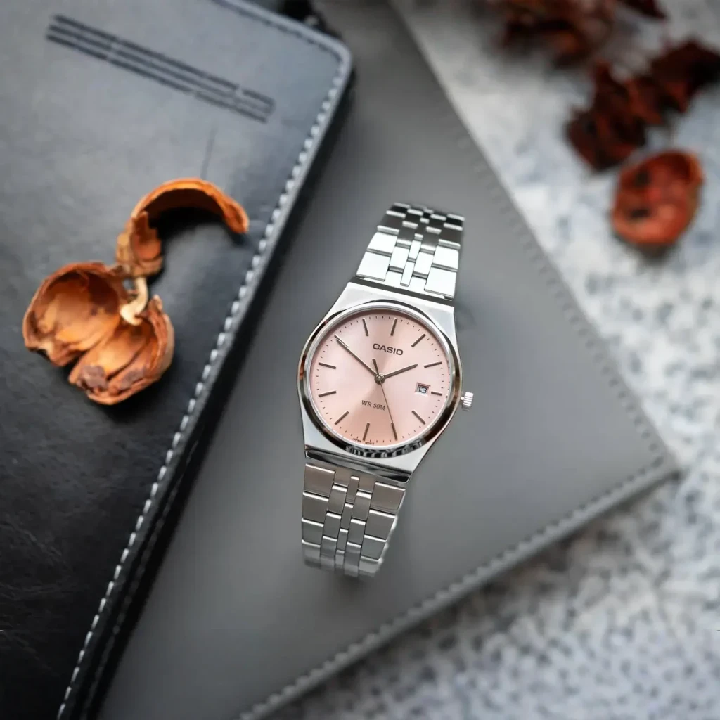 Casio MTP-B145D-4AVEF Aço Inoxidável Bateria 3 Anos 5ATM, em uso: mostrador rosa salmão sobre agenda e pinhas secas