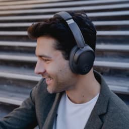 Auriculares JLab Audio IEUHBJLUXANCRGPH62 Cancelación de Ruido Diadema, uso: hombre de perfil sonriendo con auriculares