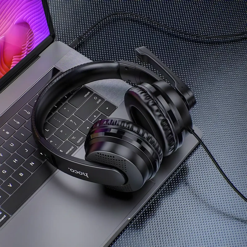 Auriculares Gaming Hoco. W103 Magic Tour con Micrófono USB-A + Jack 3,5mm, en uso: apoyados sobre teclado de laptop