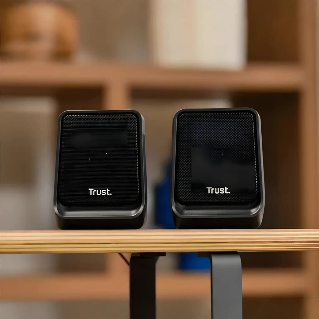 Altavoces Trust Milo 2.0 6W RMS USB en uso: par de altavoces negros sobre escritorio de madera con estantería al fondo
