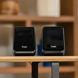 Altavoces Trust Milo 2.0 6W RMS USB en uso: par de altavoces negros sobre escritorio de madera con estantería al fondo