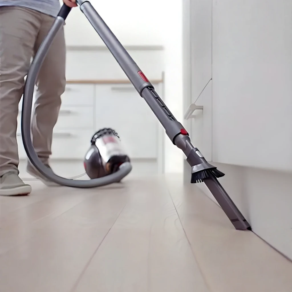 Aspiradora Dyson Big Ball Absolute 2 en uso: accesorio cepillo limpiando zócalo junto a mueble blanco en suelo laminado