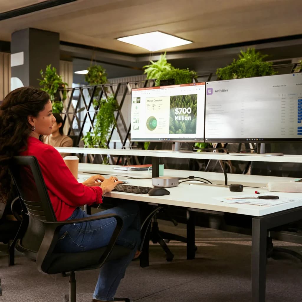 Combo Teclado y Ratón HP 725 Negro Inalámbrico Español, en uso: mujer tecleando en oficina con dos monitores y plantas
