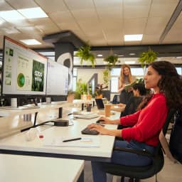 Combo Teclado y Ratón HP 725 Negro Inalámbrico Español, en uso: mujer tecleando en oficina moderna ante dos monitores