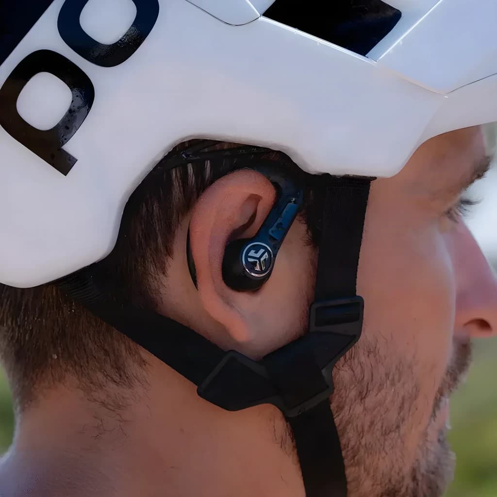 Auriculares JLab Audio Epic Sport ANC 3 Cancelación de Ruido híbrida ANC, en uso: ciclista con casco blanco lleva el earbud
