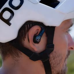 Auriculares JLab Audio Epic Sport ANC 3 Cancelación de Ruido híbrida ANC, en uso: ciclista con casco blanco lleva el earbud