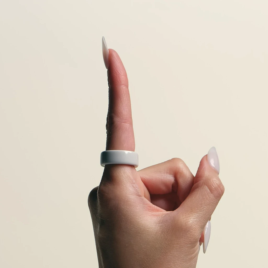 Oura Ring 4 Ceramic Talla 10 Blanco Temperatura Corporal, en uso: anillo en dedo índice levantado, acabado cerámico liso