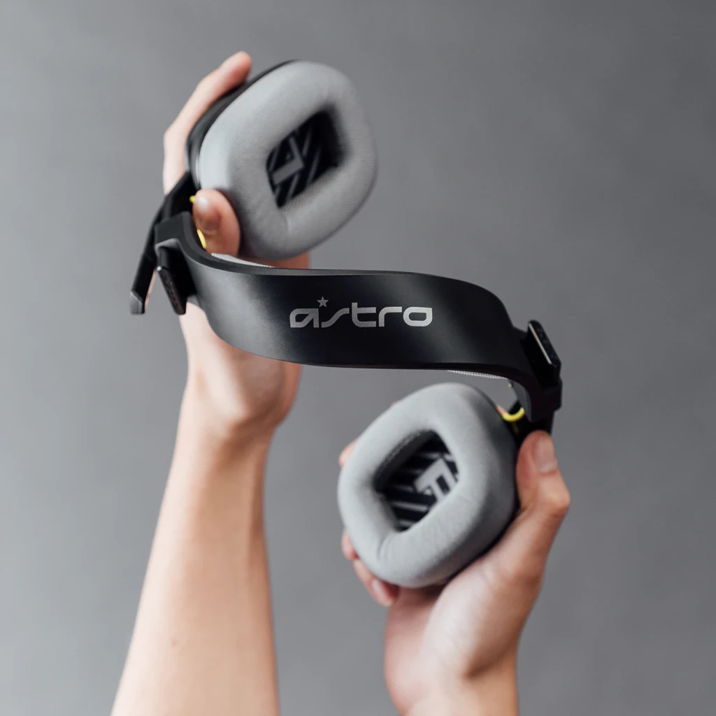 Auriculares Logitech ASTRO Gaming A10 Gen 2 con Micrófono PC/Mac/Xbox/PS, detalle: manos sostienen la diadema negra con logo
