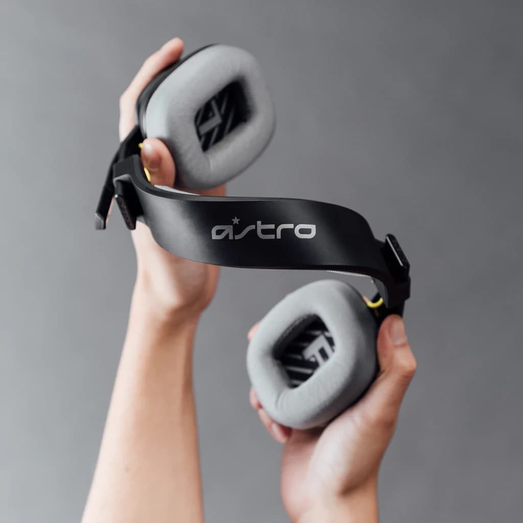 Auriculares Logitech ASTRO Gaming A10 Gen 2 con Micrófono PC/Mac/Xbox/PS, detalle: manos sostienen la diadema negra con logo