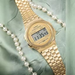 Casio Vintage A171WEG-9AEF Batterie 7 Ans Résistante à l'eau, porté: montre dorée sur tissu vert avec collier de perles