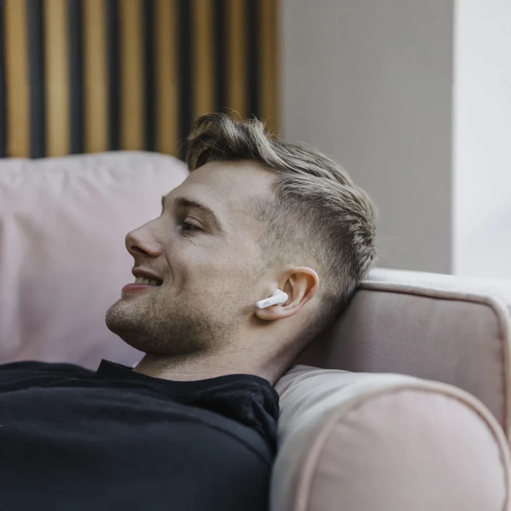 Écouteurs JVC HA-A3T TWS Bluetooth 5.1 22h IPX4 en utilisation: homme allongé sur canapé avec écouteur blanc dans l'oreille