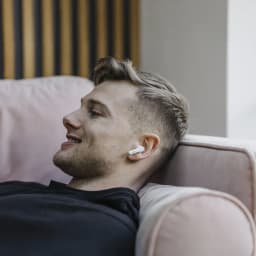 Écouteurs JVC HA-A3T TWS Bluetooth 5.1 22h IPX4 en utilisation: homme allongé sur canapé avec écouteur blanc dans l'oreille