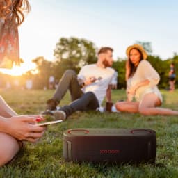 Altavoz portátil LG XBoom Bounce by will.i.am 2.1 IP67 40W 30h Bluetooth 5.3, en uso: sobre hierba en parque al atardecer