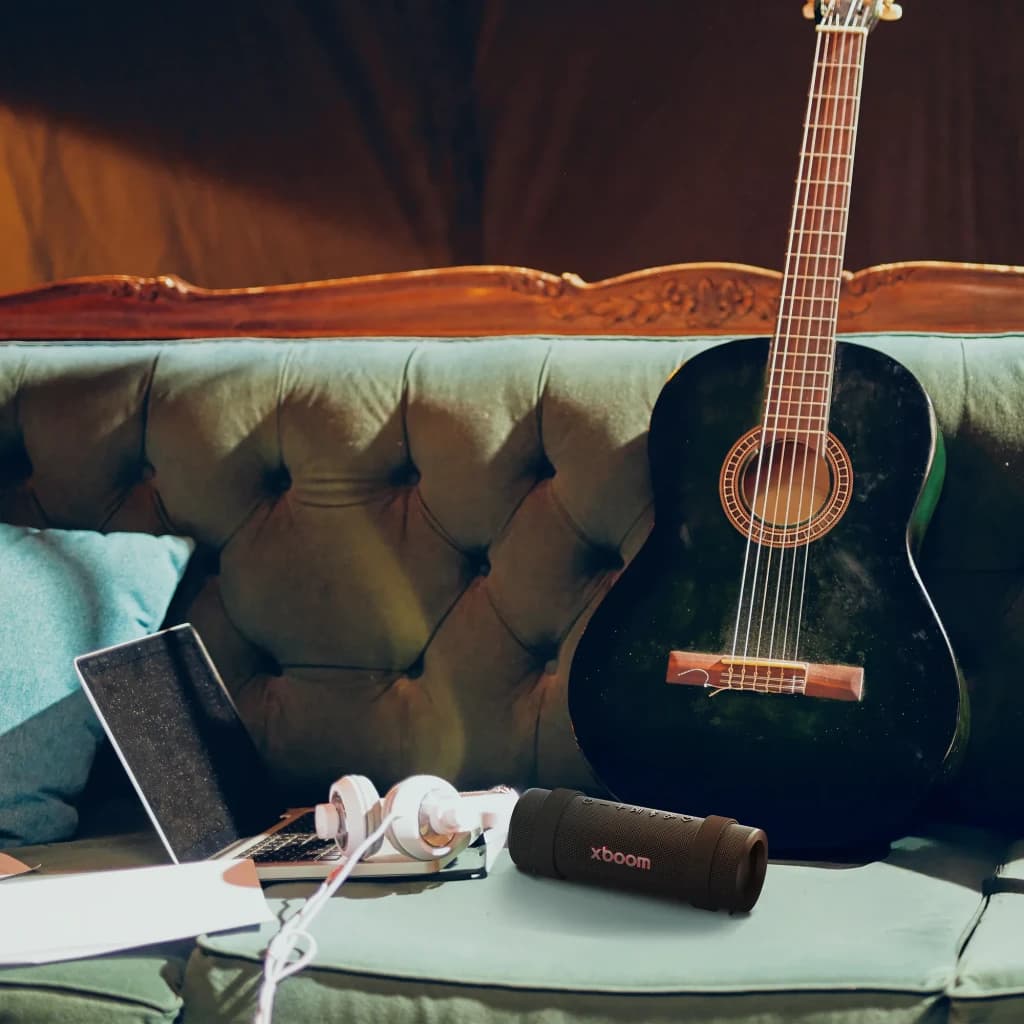 Altavoz portátil LG XBOOM Grab by will.i.am IP67 30W 20h Bluetooth 5.3, en uso: sobre sofá vintage junto a guitarra