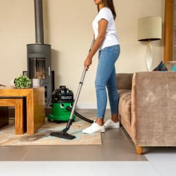 Aspirateur cylindrique Numatic GVE370-2 Vert 1000W Sec et humide, en usage: femme aspire tapis dans salon avec cheminée
