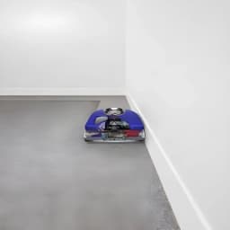 Robot aspirador Dyson 360 Vis Nav Sensor de infravermelhos 65min, em uso: a limpar junto a um rodapé em chão cinzento