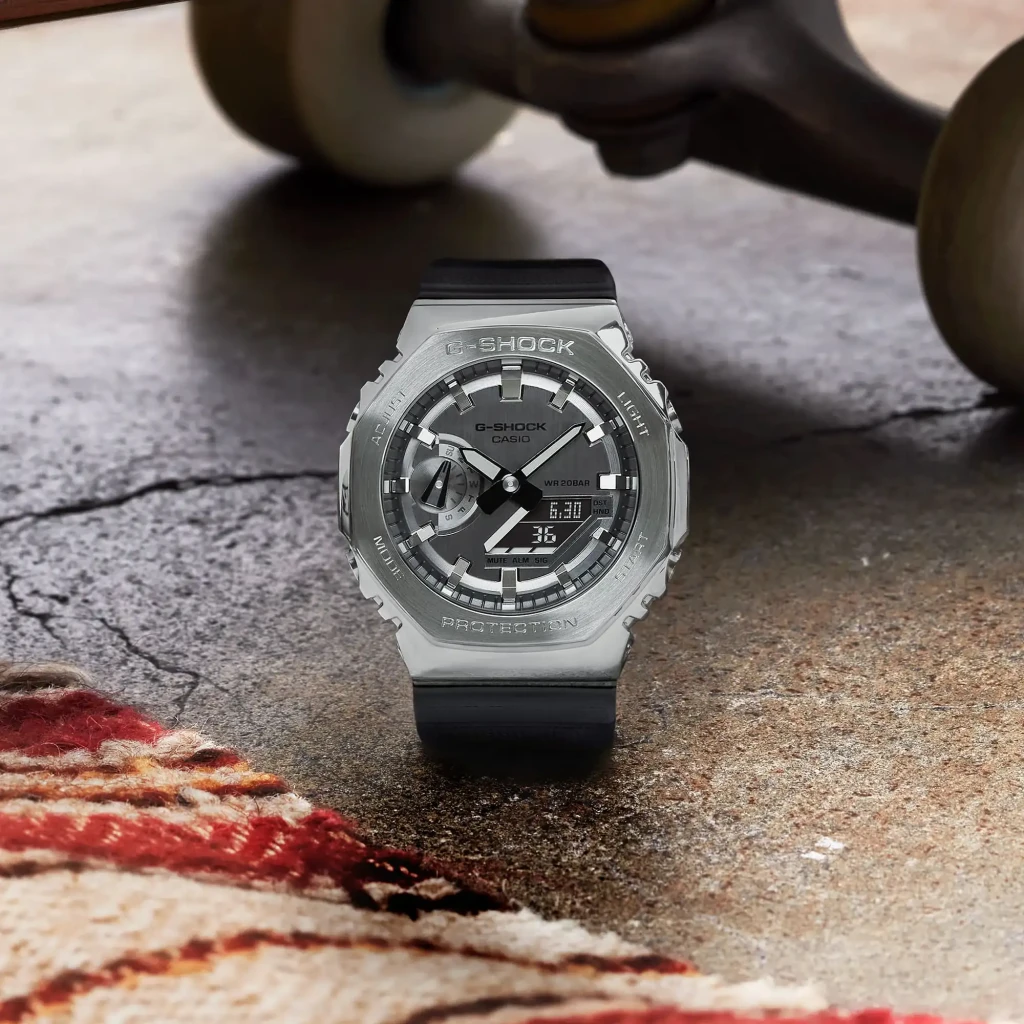 Casio G-Shock GM-2100-1A Preto Bateria 2 Anos Prata 20ATM, em uso: relógio sobre superfície de cimento rachado com skate