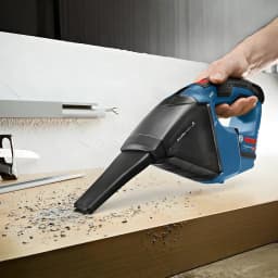 Aspirador de mão Bosch GAS 12V Preto/Azul Sem Fios 900l/min, em uso: mão segurando o aspirador a recolher aparas de madeira