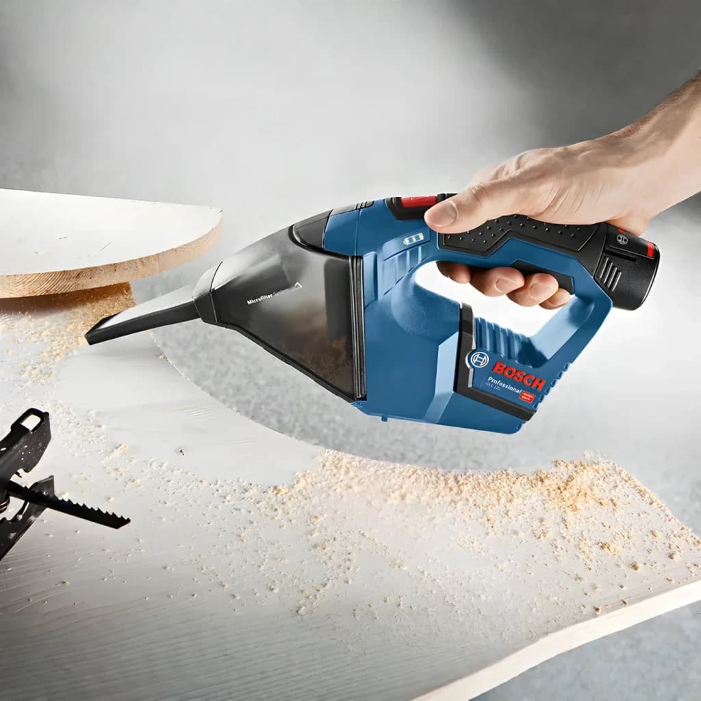 Aspirador de mão Bosch GAS 12V Preto/Azul Sem Fios 900l/min, em uso: mão aspirando serradura de madeira em superfície