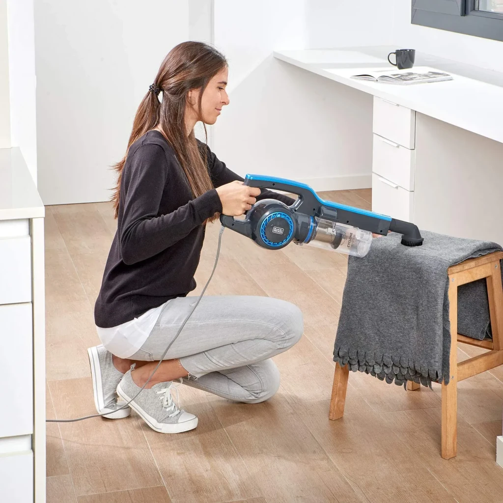 Aspirateur balai Black & Decker 3 en 1 Noir 600W Câble 6m BXVMS600E, usage main: femme aspire un tabouret avec l'unité