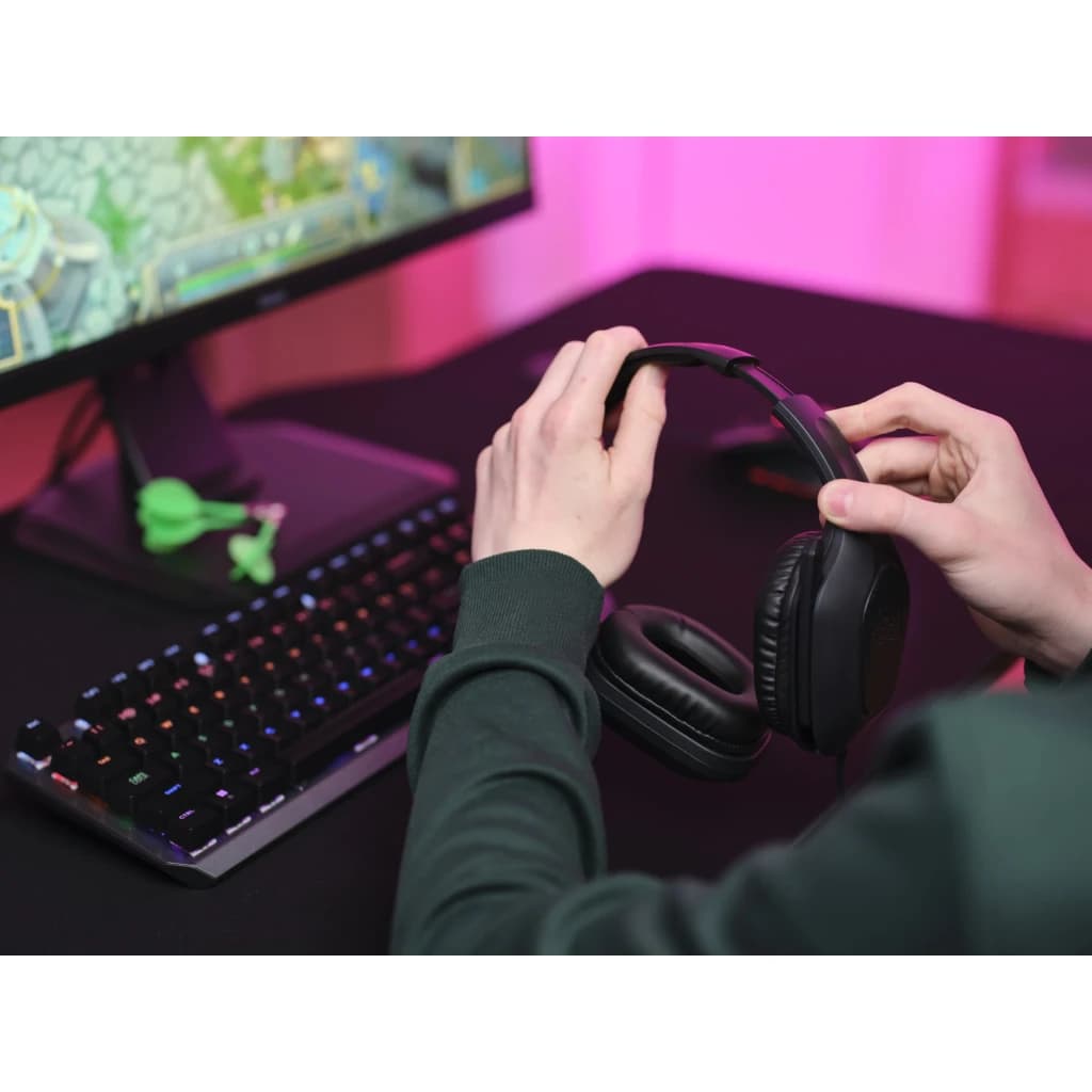 Casque Gaming Trust GXT 415 Zirox Microphone Boom Noir - mains tenant le casque sur bureau gaming avec clavier RGB