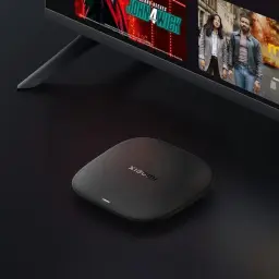 Xiaomi TV Box S 3rd Gen 4K negro mate, diseño compacto cuadrado con bordes redondeados, LED frontal blanco, junto a TV; mando negro con botones de color