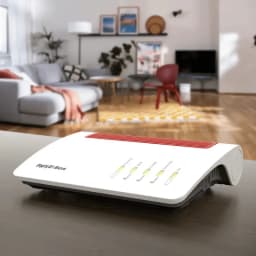 Router FRITZ!Box 5590 Fiber WiFi 6 na cor branca com grade vermelha, LEDs de estado frontais e design curvo, colocado sobre uma mesa em uma sala moderna