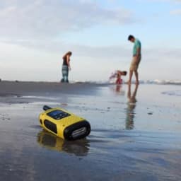 Talkie-walkie jaune Motorola T92 H2O posé sur plage mouillée, boîtier robuste antichoc, accents noirs, écran et bouton poussoir visibles, conçu pour