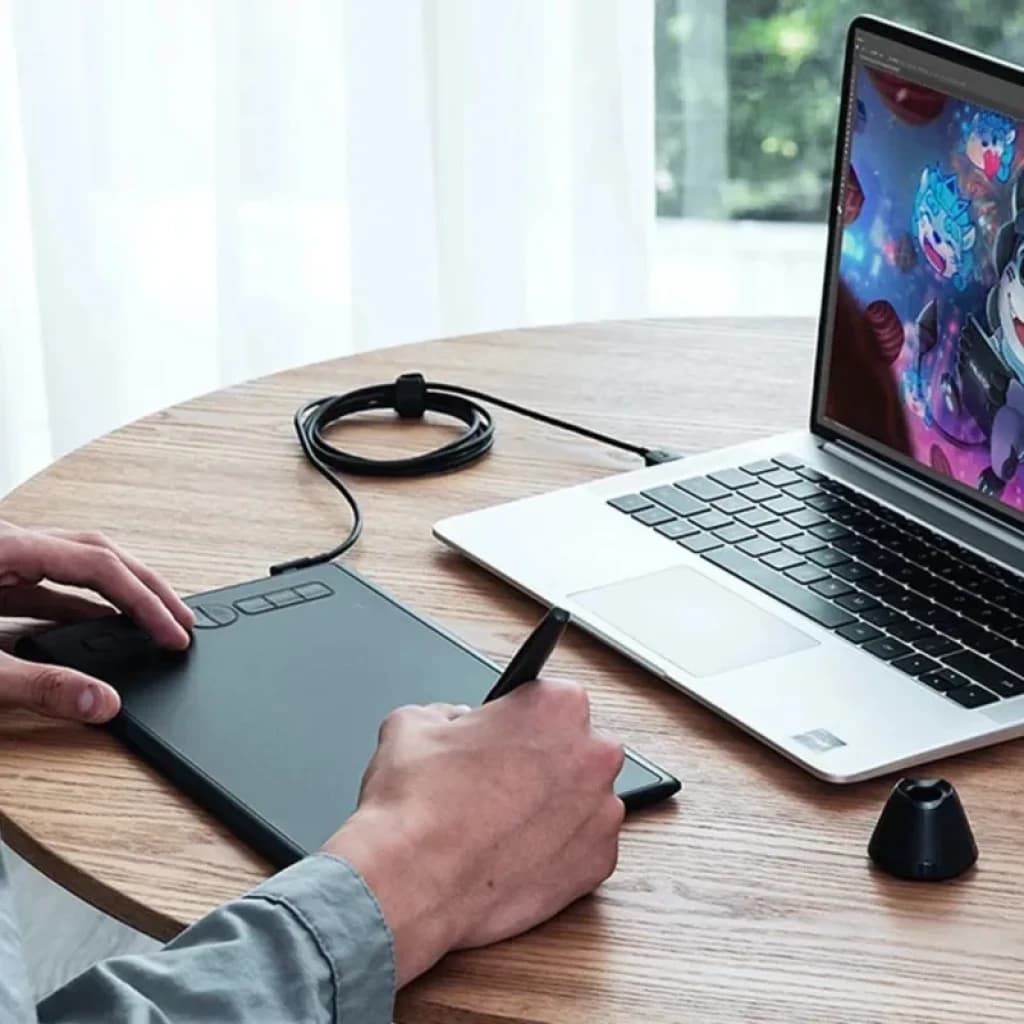 Huion H580X con 8 teclas programables: tableta gráfica negra compacta, lápiz sin batería, base para lápiz y conexión por cable junto a laptop en uso