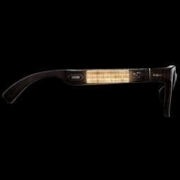 Xiaomi AI Glasses, vista lateral: patilla negra con módulo rectangular transparente iluminado, botón ovalado y logo Xiaomi cerca de la bisagra