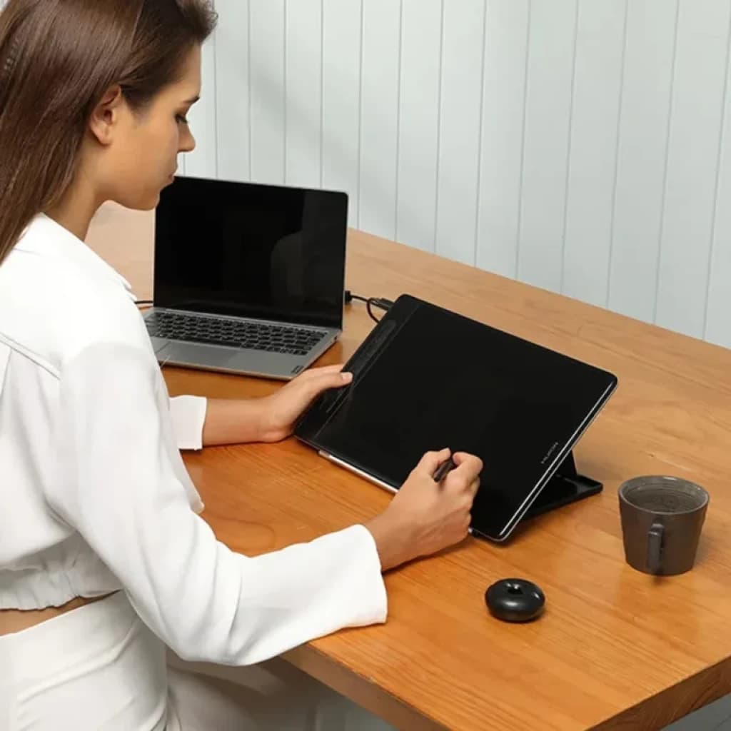Huion Kamvas Pro 13 GT1302 avec écran IPS 13,3 pouces 2,5K QHD+, stylet en main, support inclinable, connectée à un laptop sur bureau en bois