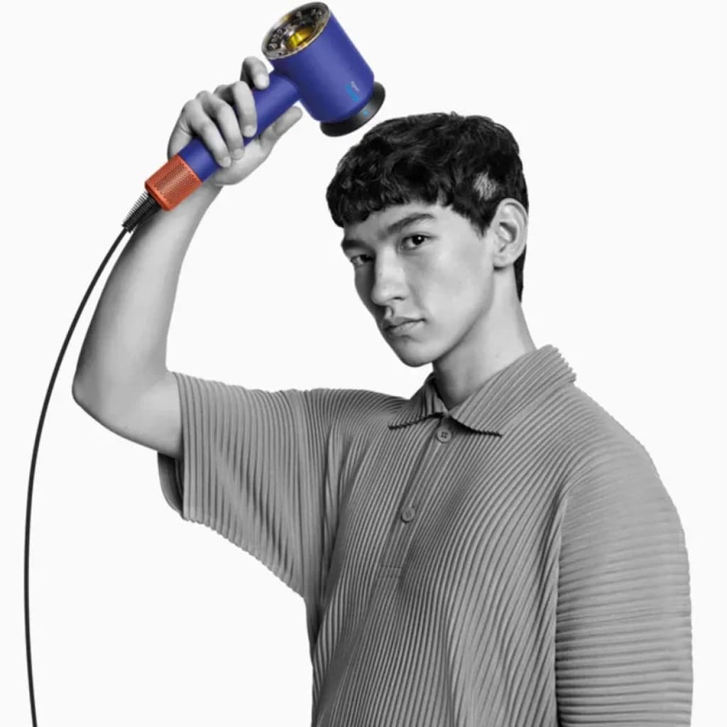 Dyson Supersonic Nural HD16 Ceramic Blue secador con cuerpo azul cerámico, rejilla dorada visible y cable negro, mostrado en uso sobre la cabeza