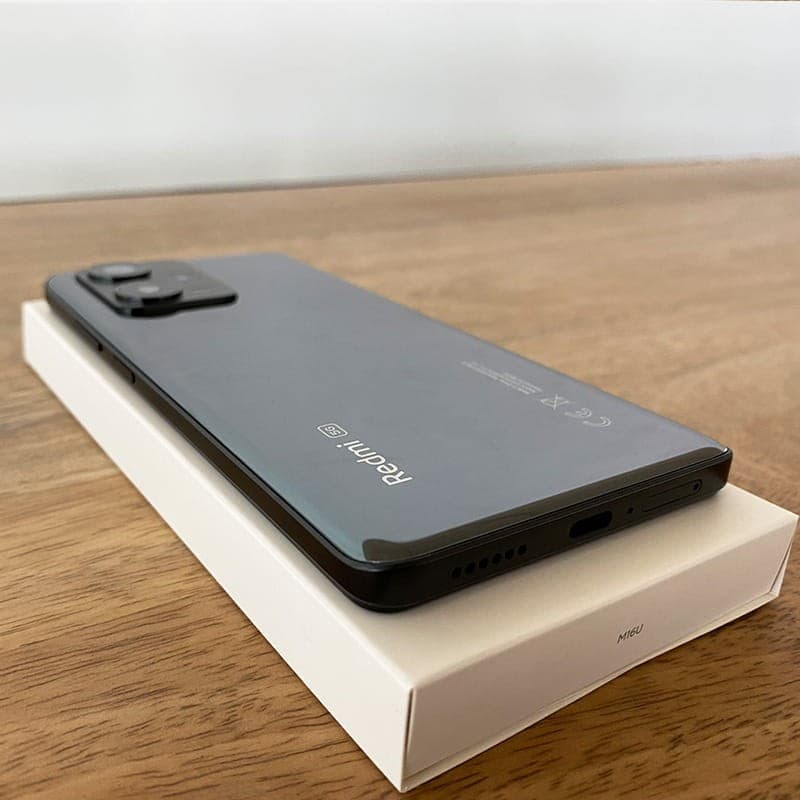 Smartphone Xiaomi Redmi Note 12 Pro+ 5G preto sobre caixa branca, traseira brilhante com módulo de câmera saliente e porta USB-C na base, classe B